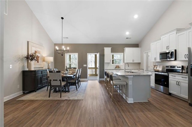 kitchen featuring appliances with stainless steel finishes, a sink, high vaulted ceiling, white cabinetry, and backsplash