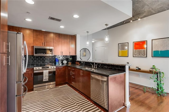 kitchen featuring stainless steel appliances, a peninsula, a sink, visible vents, and backsplash