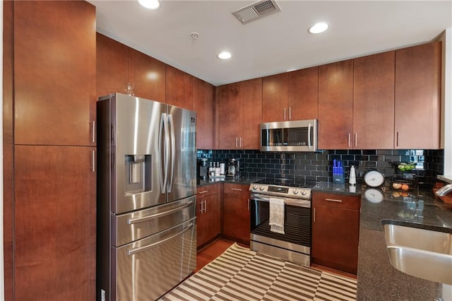 kitchen with visible vents, decorative backsplash, appliances with stainless steel finishes, a sink, and dark stone counters