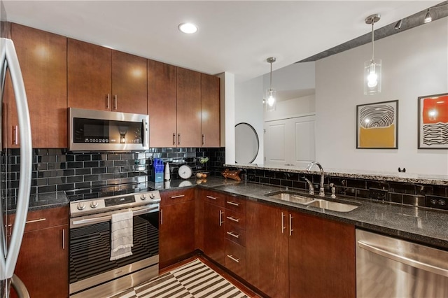 kitchen featuring a sink, appliances with stainless steel finishes, tasteful backsplash, dark stone countertops, and pendant lighting