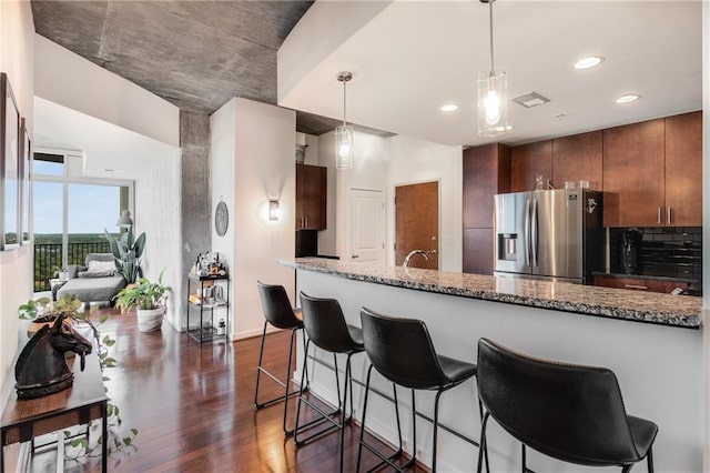 kitchen with stainless steel fridge, stone countertops, brown cabinetry, dark wood finished floors, and a kitchen breakfast bar