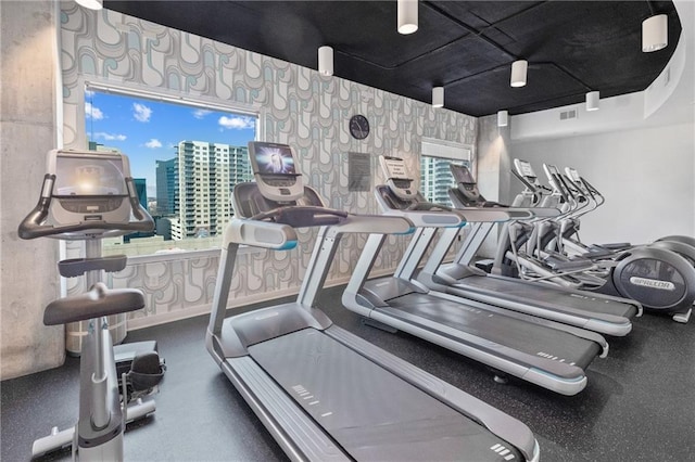 gym featuring a healthy amount of sunlight, wallpapered walls, visible vents, and a city view