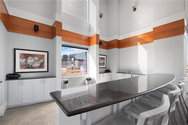 interior space with a high ceiling, dark stone counters, a kitchen breakfast bar, and light tile patterned flooring