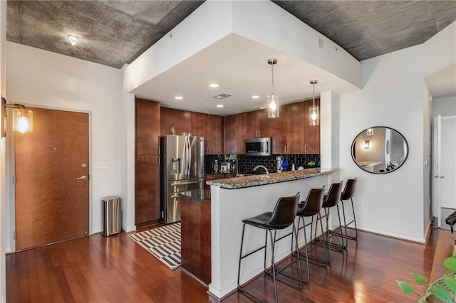 kitchen featuring stainless steel appliances, dark wood-style flooring, a peninsula, and backsplash