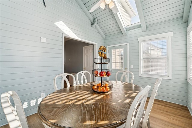 dining room featuring light hardwood / wood-style floors, lofted ceiling with skylight, ceiling fan, and wood walls