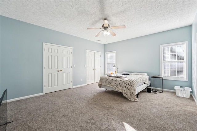 bedroom with carpet flooring, ceiling fan, a textured ceiling, and two closets