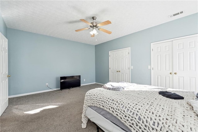 bedroom with carpet flooring, a textured ceiling, ceiling fan, and multiple closets