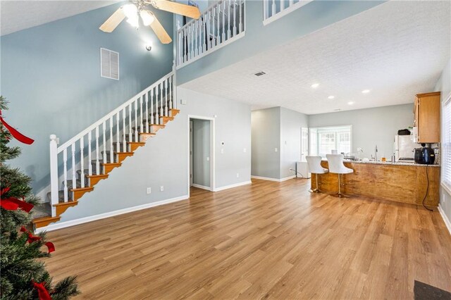 living room with ceiling fan, light hardwood / wood-style floors, and a towering ceiling