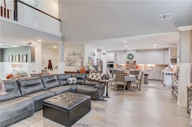 living room featuring light wood-type flooring, a high ceiling, and ornate columns