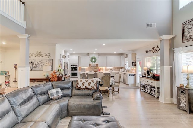 living room with a towering ceiling, light hardwood / wood-style flooring, and ornate columns