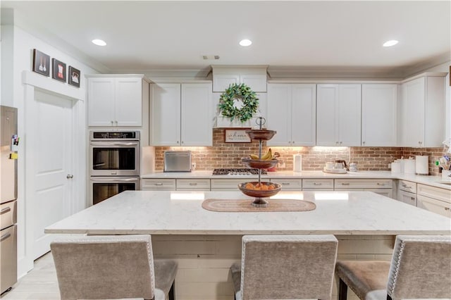 kitchen with a breakfast bar, appliances with stainless steel finishes, light stone counters, white cabinets, and a kitchen island