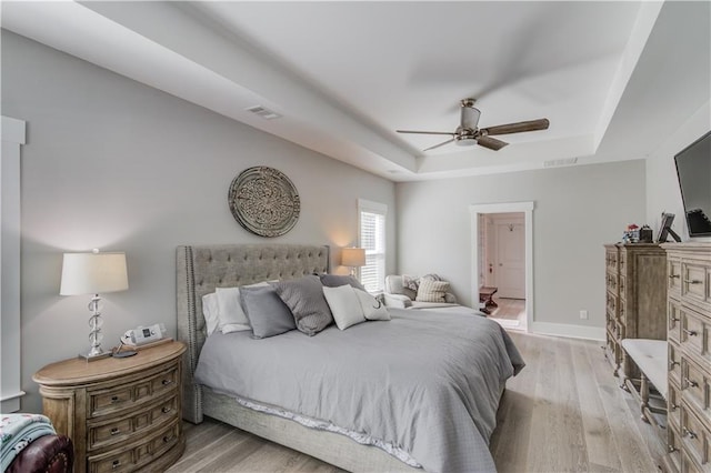 bedroom with ceiling fan, a raised ceiling, and light hardwood / wood-style flooring