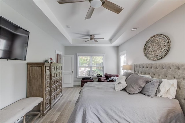 bedroom featuring ceiling fan, a tray ceiling, and light hardwood / wood-style floors