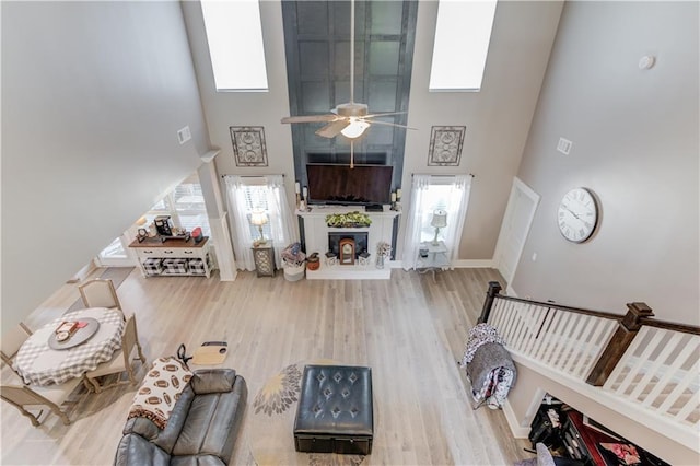 living room with wood-type flooring, a large fireplace, ceiling fan, and a high ceiling