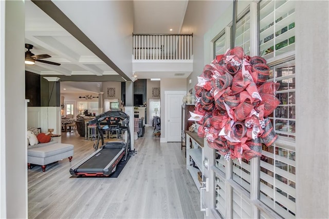 interior space with coffered ceiling, a high ceiling, ceiling fan, and light wood-type flooring