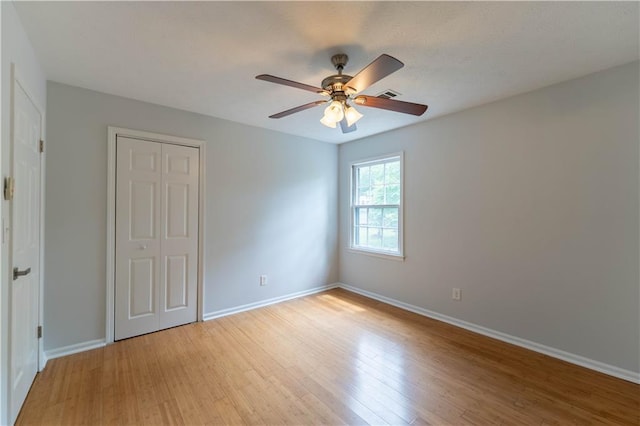 unfurnished bedroom featuring light wood finished floors, baseboards, a closet, and ceiling fan