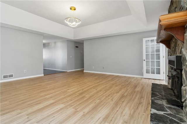 unfurnished living room with a tray ceiling, wood finished floors, a fireplace with raised hearth, and visible vents