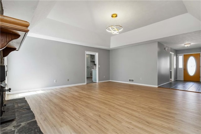 unfurnished living room featuring visible vents, baseboards, a tray ceiling, and wood finished floors