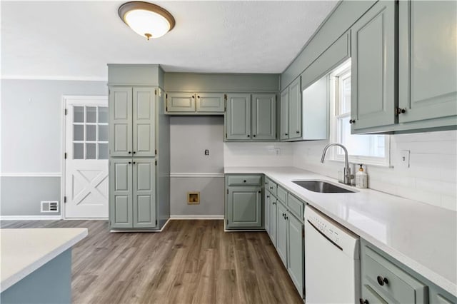 kitchen with baseboards, light countertops, dark wood-style flooring, white dishwasher, and a sink