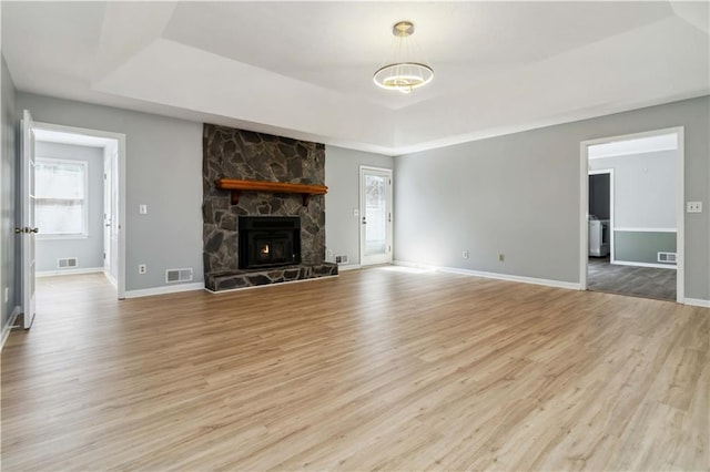 unfurnished living room with a tray ceiling, baseboards, light wood-style floors, and visible vents