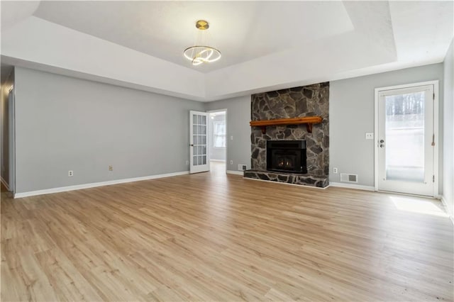 unfurnished living room with visible vents, a tray ceiling, a fireplace, light wood finished floors, and baseboards