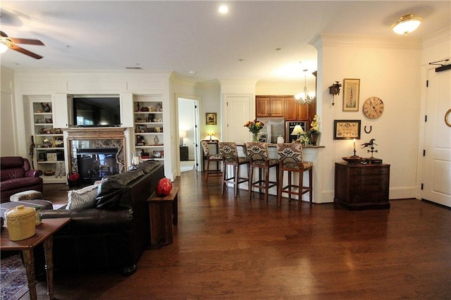 living room featuring ornamental molding, dark hardwood / wood-style flooring, built in features, a high end fireplace, and ceiling fan with notable chandelier