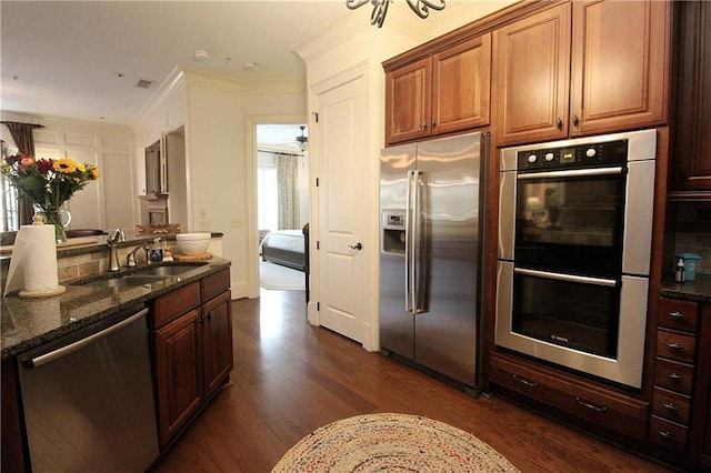 kitchen with sink, crown molding, dark stone countertops, appliances with stainless steel finishes, and dark hardwood / wood-style flooring