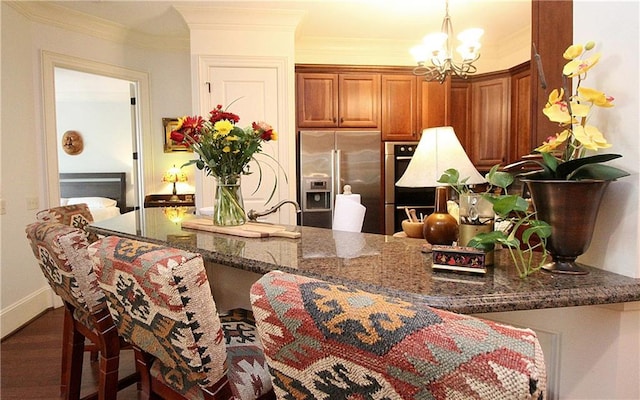 kitchen with pendant lighting, dark stone countertops, stainless steel fridge, a notable chandelier, and crown molding