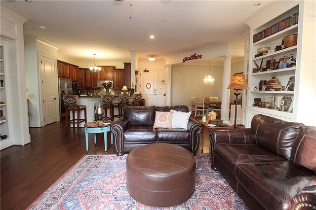 living room featuring an inviting chandelier, dark wood-type flooring, built in features, and ornate columns