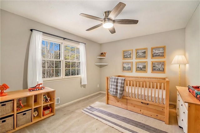 bedroom with a crib, light colored carpet, and ceiling fan