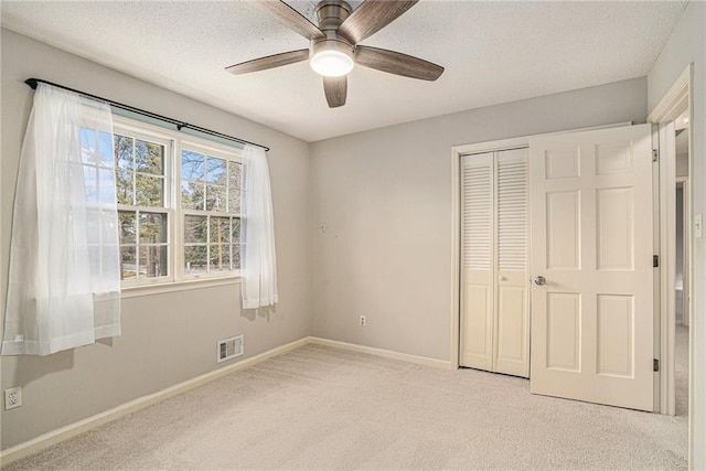 unfurnished bedroom featuring light carpet, ceiling fan, a closet, and a textured ceiling