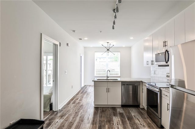 kitchen featuring track lighting, dark wood-style flooring, a peninsula, a sink, and appliances with stainless steel finishes