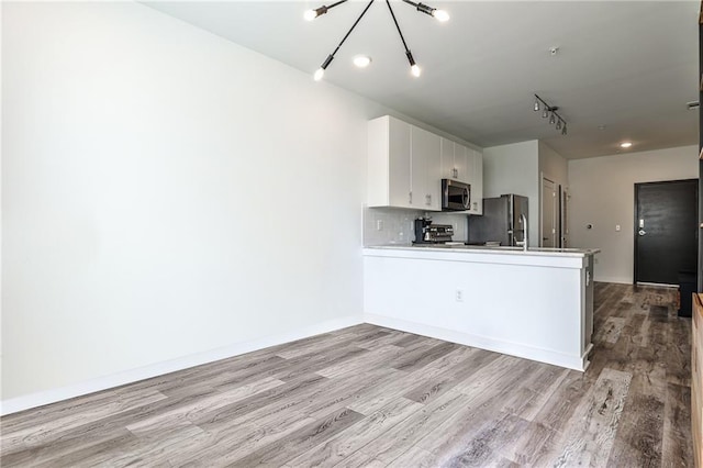 kitchen with appliances with stainless steel finishes, wood finished floors, light countertops, a peninsula, and white cabinetry