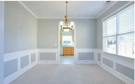 spare room featuring a chandelier, light carpet, and crown molding