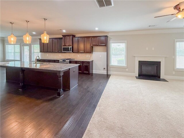 kitchen featuring sink, appliances with stainless steel finishes, hanging light fixtures, light stone countertops, and an island with sink