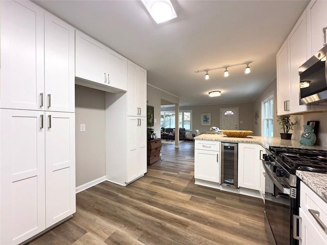 kitchen with white cabinetry, kitchen peninsula, appliances with stainless steel finishes, wine cooler, and light stone counters