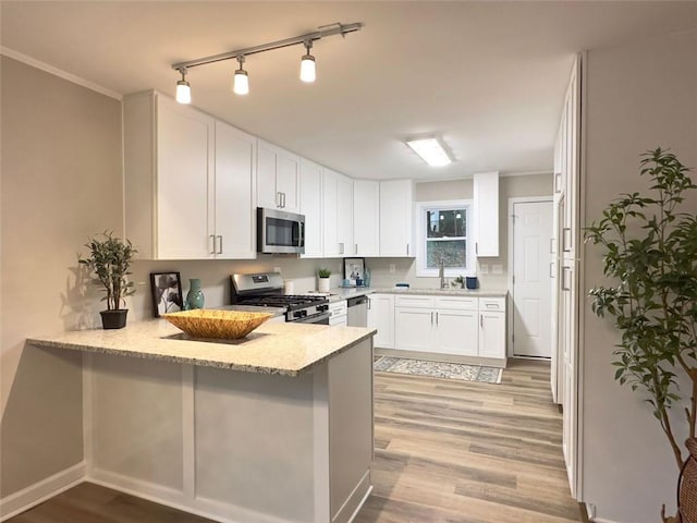 kitchen with white cabinetry, kitchen peninsula, stainless steel appliances, light stone countertops, and light hardwood / wood-style flooring