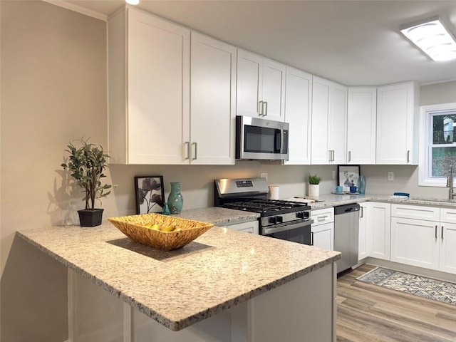 kitchen featuring light hardwood / wood-style floors, kitchen peninsula, stainless steel appliances, light stone countertops, and white cabinets