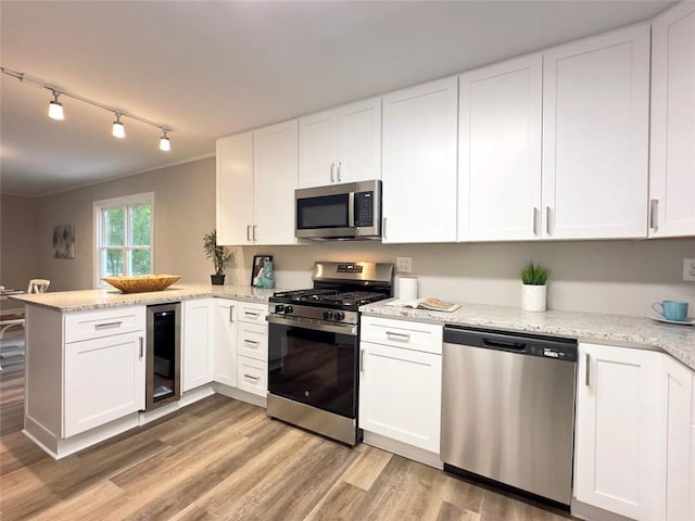 kitchen with kitchen peninsula, appliances with stainless steel finishes, light wood-type flooring, wine cooler, and white cabinets