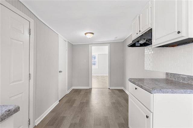 kitchen featuring white cabinets, light wood-type flooring, crown molding, and backsplash