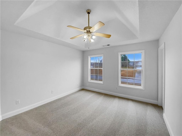 empty room with carpet flooring, a raised ceiling, visible vents, and baseboards