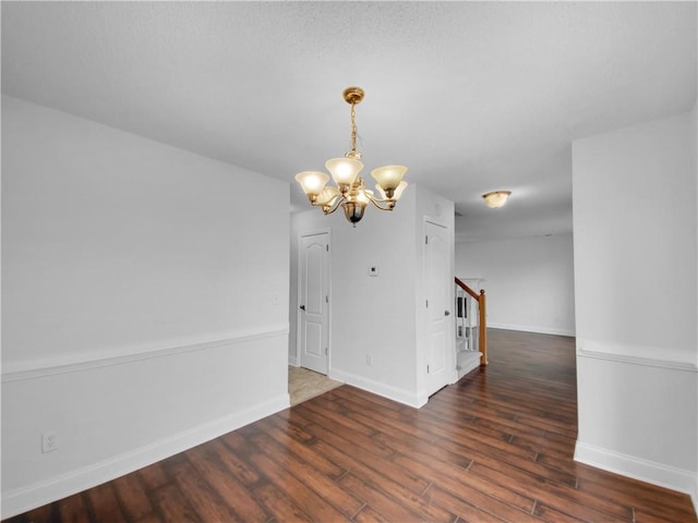 empty room featuring an inviting chandelier, baseboards, stairway, and wood finished floors