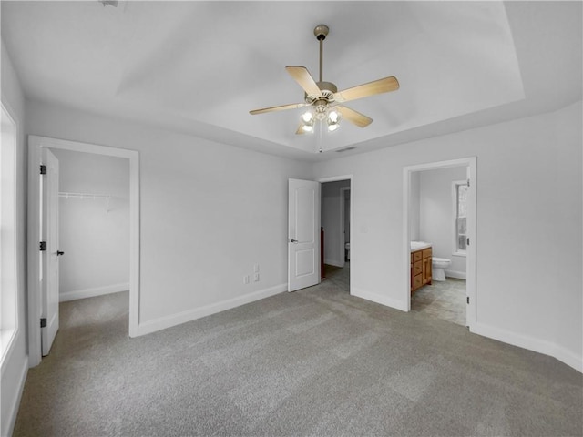 unfurnished bedroom with ensuite bathroom, light carpet, baseboards, a spacious closet, and a tray ceiling