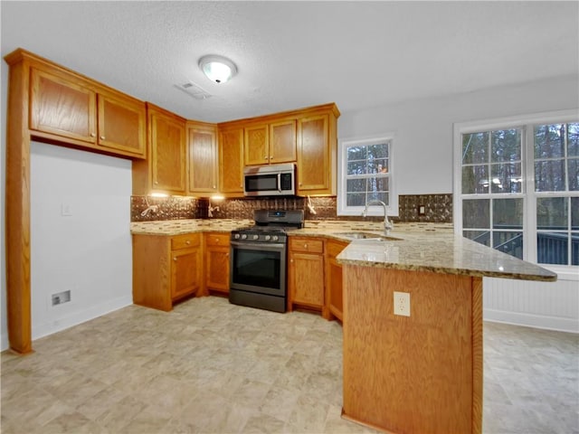 kitchen with appliances with stainless steel finishes, brown cabinetry, a sink, light stone countertops, and a peninsula