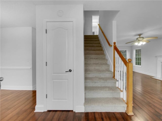 staircase featuring a fireplace with flush hearth, ceiling fan, baseboards, and wood finished floors