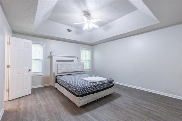 bedroom featuring a tray ceiling, baseboards, wood finished floors, a textured ceiling, and ceiling fan