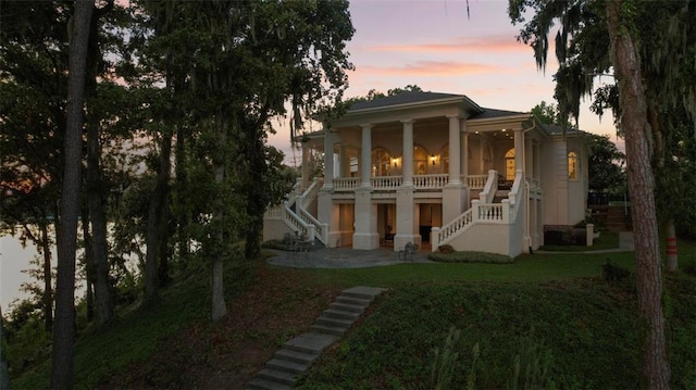 back house at dusk featuring a yard, covered porch, and a patio area