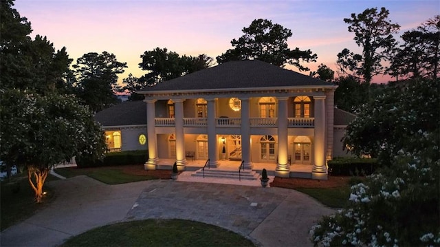 back house at dusk with french doors, a balcony, and a patio