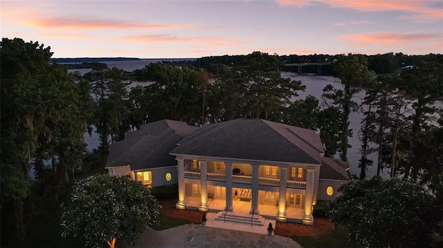 back house at dusk featuring a balcony and a water view