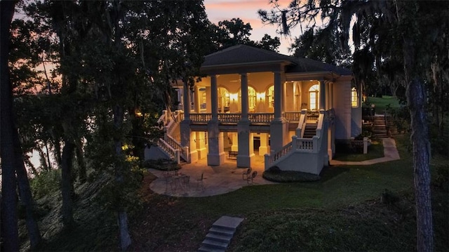 back house at dusk featuring a lawn and a patio